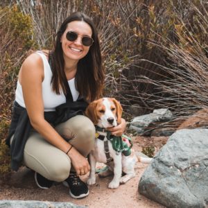 woman in white tank top sitting beside brown and white short coated dog