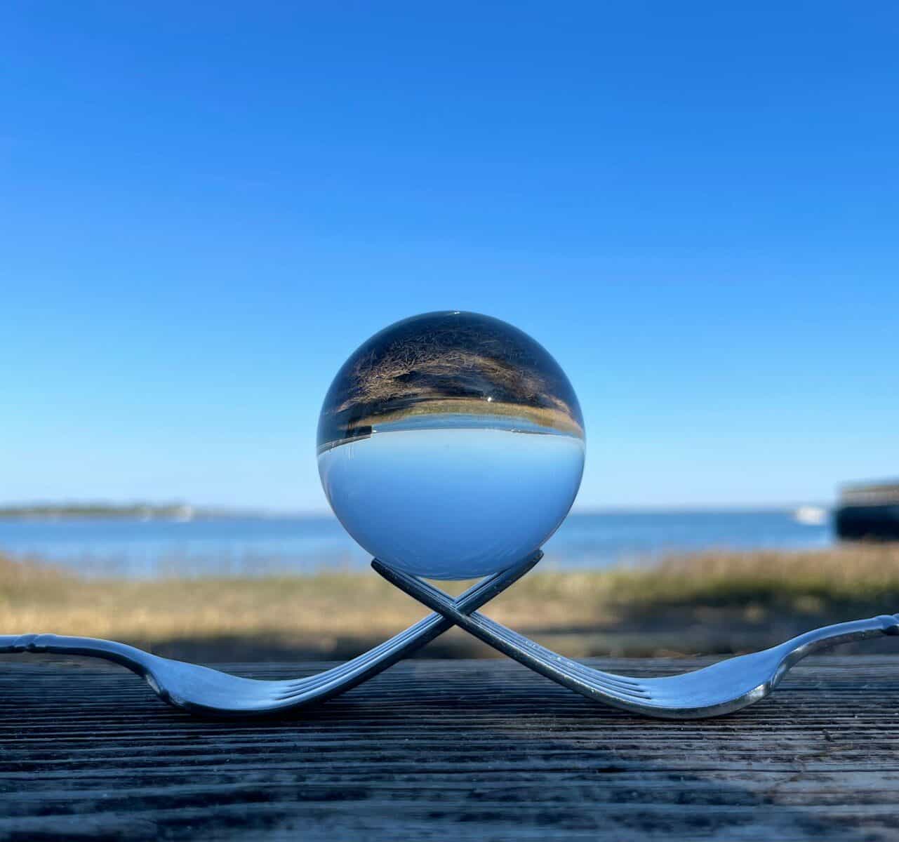Crystal ball on forks reflects ocean and sky.